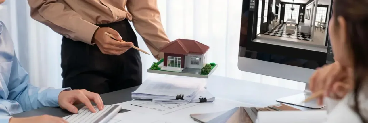 Agent pointing to a model house on a desk during a planning meeting